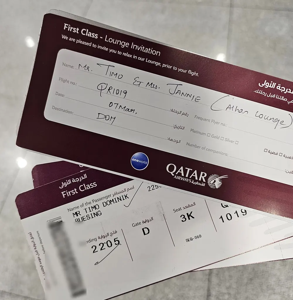 Bordkarte der Qatar First Class und handschriftlich ausgefüllte Loungeeinladung für Doha, der Barcode ist verwischt.