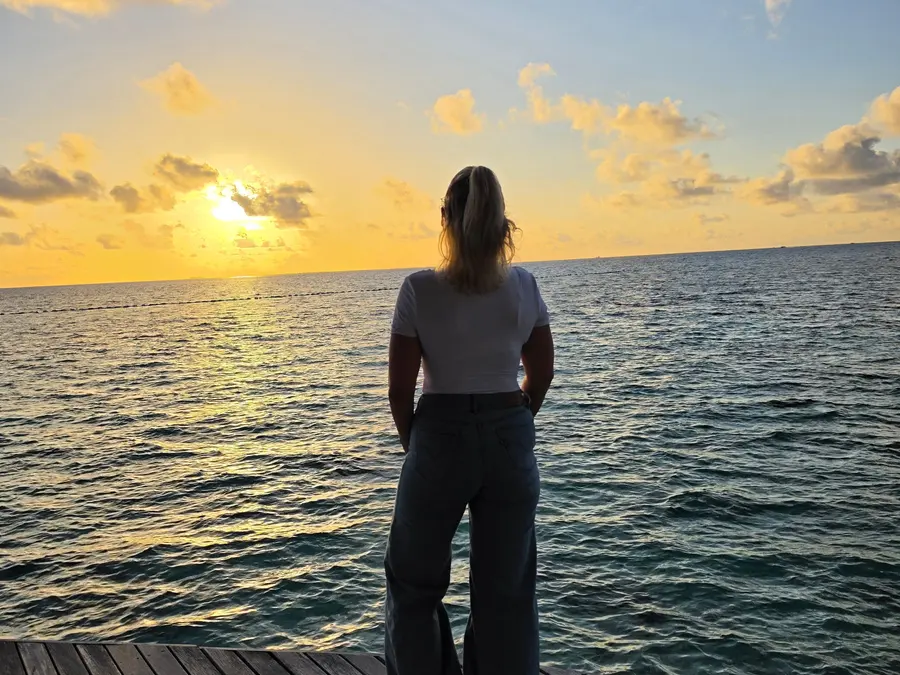 Janine steht von hinten auf einem Holzsteg und schaut bei Sonnenuntergang auf das Meer der Malediven.