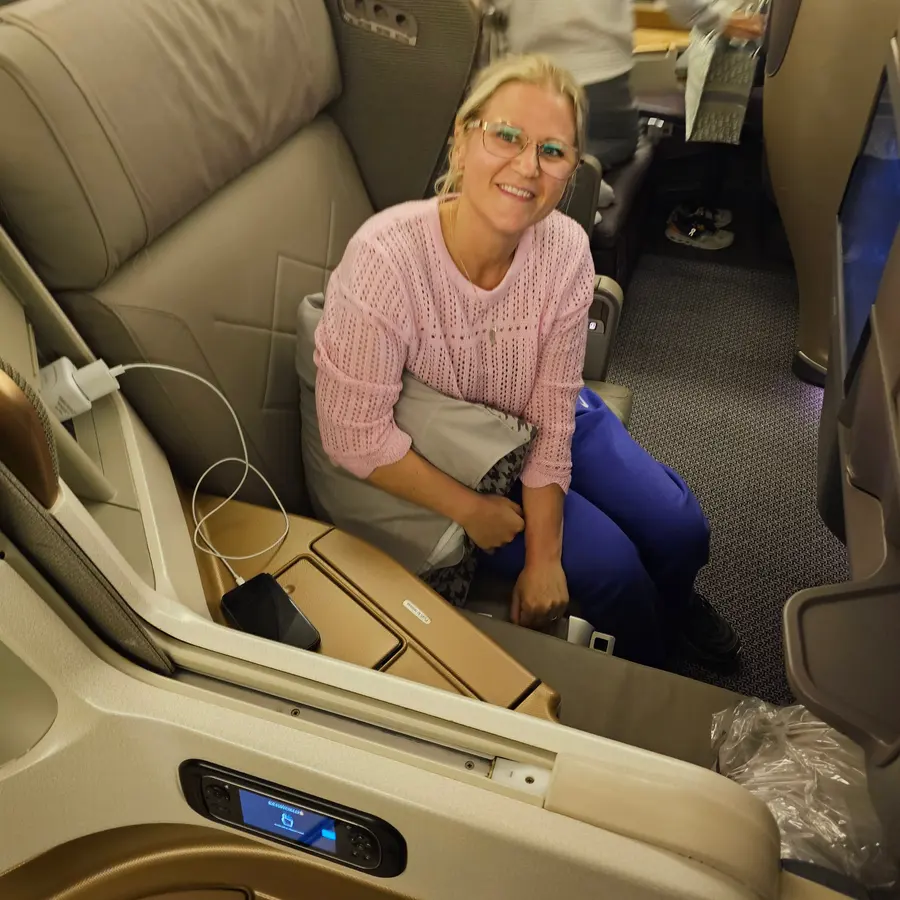 Janine sitzt lächelnd in einem beigen Business Sitz von Singapore Airlines, vor ihr die Fußablage.